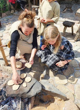 Kvinde og barn laver brød ved bålet på Hvolris Jernalder