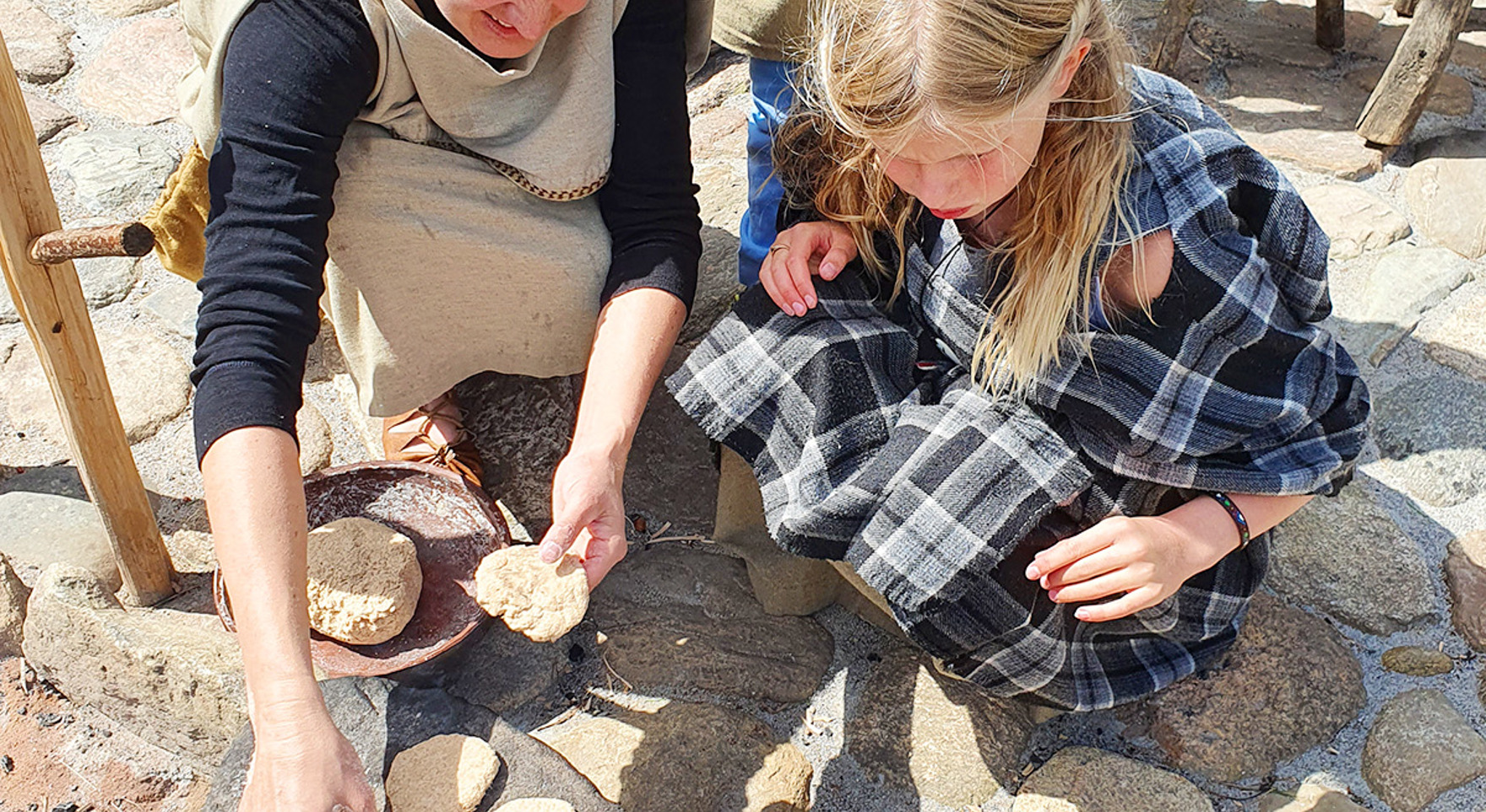 Kvinde og barn laver brød ved bålet på Hvolris Jernalder